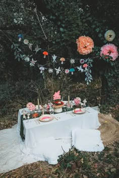 a table set up with flowers and plates on it for an outdoor dinner party in the woods