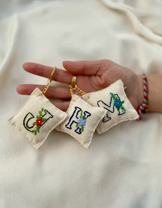 someone is holding two small embroidered keychains in their left hand, one with the letter e on it