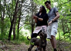 a man and woman standing next to a dog in the woods