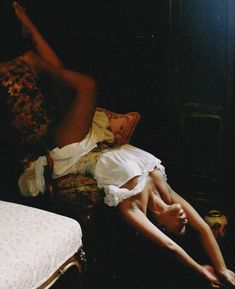 a woman laying on top of a bed next to a white pillow and chair in a dark room