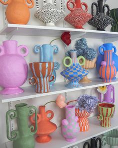 many different vases are on shelves in a room that is white and has various colors