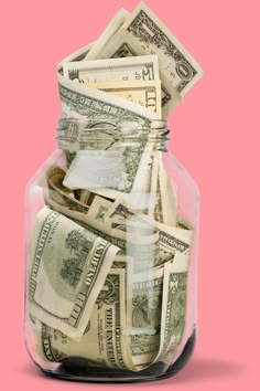 a glass jar filled with money on top of a pink background