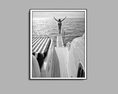 a black and white photo of a person standing on the back of a boat in the ocean