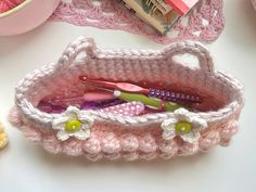 a crocheted pink purse with toothbrushes and other items in it on a table