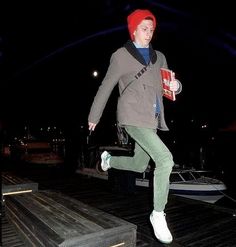 a man with red hair is jumping on the dock and holding a book in his hand