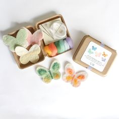 an open box filled with lots of different colored felt butterflies next to a package of yarn