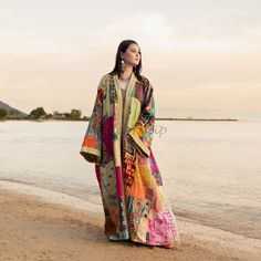 a woman standing on top of a sandy beach next to the ocean wearing a colorful dress