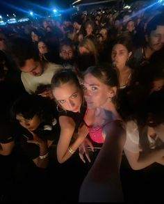 two young women standing next to each other in front of a crowd at a concert