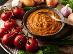 a bowl of tomato sauce with some tomatoes and garlic on the side next to it