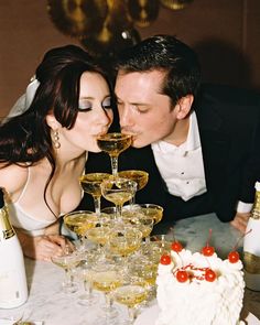 a man and woman kissing in front of a cake with wine glasses on it,