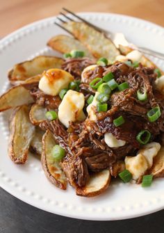 a white plate topped with meat and potatoes on top of a wooden table next to a fork