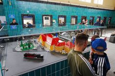 two boys looking at a model train set in a building with people standing around it