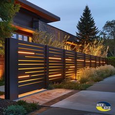 a modern house with lights on the side of it's fence and trees in the background