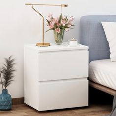 a white nightstand next to a bed with pink flowers on it and a blue headboard