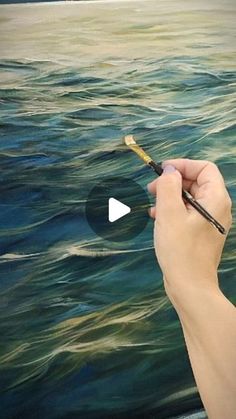 a person is holding a paintbrush in their hand and painting an ocean scene on the canvas