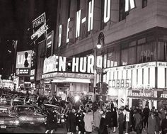 black and white photograph of people walking on the sidewalk in front of a building at night