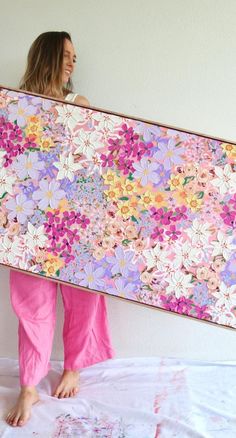 a woman holding up a large painting with pink and purple flowers on it's side