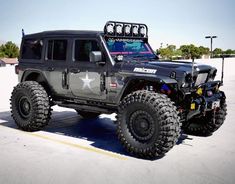 a black jeep is parked in a parking lot with two large tires on it's sides