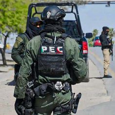 two police officers walking down the street in front of a car and another person standing behind them