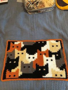 a crocheted cat rug on a bed next to a plastic container with yarn