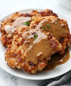 three chicken patties covered in gravy on a white plate