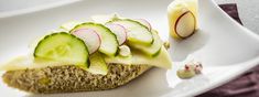 a piece of bread topped with cucumbers and radishes on a white plate