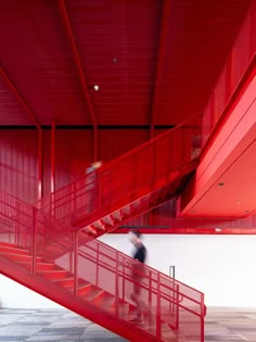 a man walking down a red staircase next to a white wall and metal railings