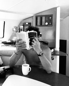 a man reading a book while sitting at a table in front of a coffee cup