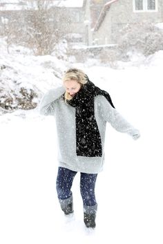 a woman walking through the snow in front of a house