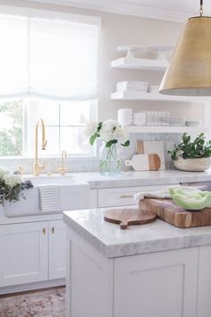 a white kitchen with marble counter tops and gold pendant light hanging over the stove top