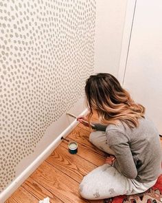 a woman sitting on the floor painting a wall