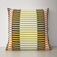 an orange and green striped pillow sitting on top of a white floor next to a wall