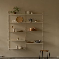 a shelf with various items on it and a stool next to it in front of the wall