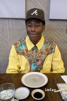 a man wearing a hat sitting at a table with plates and drinks in front of him