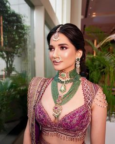 a woman in a purple and green outfit with jewelry on her neck, posing for the camera