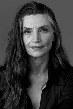 an older woman with long hair posing for a black and white photo in front of a gray background