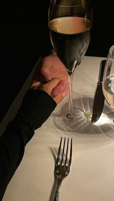 two people holding hands over a table with wine and silverware in front of them