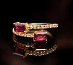 two gold rings with red and white stones on black reflective surface, close up view