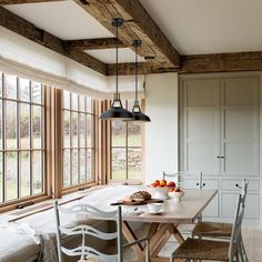 a dining room table and chairs in front of large windows with wooden beams on the ceiling