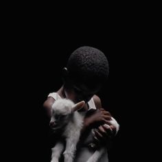 a young boy holding a baby lamb in his arms and looking at the camera, against a black background