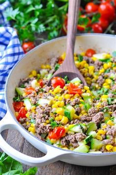 a skillet filled with meat and vegetables on top of a wooden table next to tomatoes