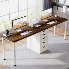 a computer desk with two monitors on top of it in front of a large window