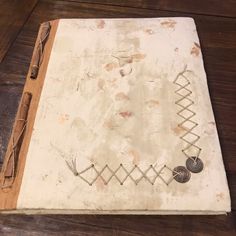 an old book with wire work on it sitting on a wooden table next to a pair of scissors