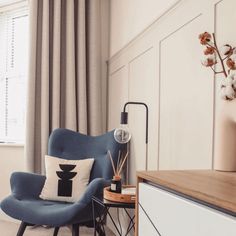 a blue chair sitting next to a window in a room with white walls and curtains