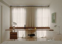 a bedroom with a bed, desk and window in the corner that has sheer curtains