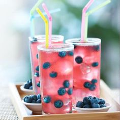 three glasses filled with blueberries and lemonade on top of a wooden tray next to strawberries