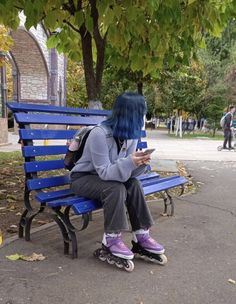 a woman with blue hair sitting on a bench looking at her cell phone while wearing roller skates