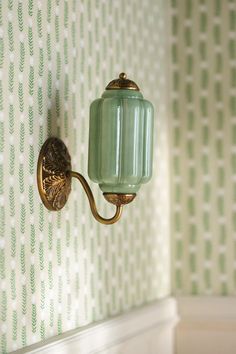 a green glass light fixture on a wall in a room with white and green wallpaper