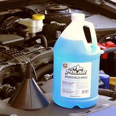 a gallon of windshield wash sitting on the hood of a car next to an engine