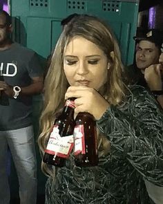 a woman is holding two beer bottles in front of her face while others look on